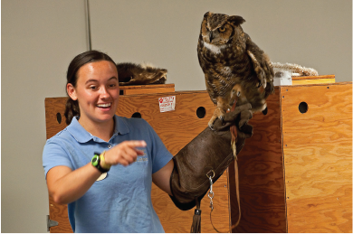Woman holding an owl and talking to an audience.